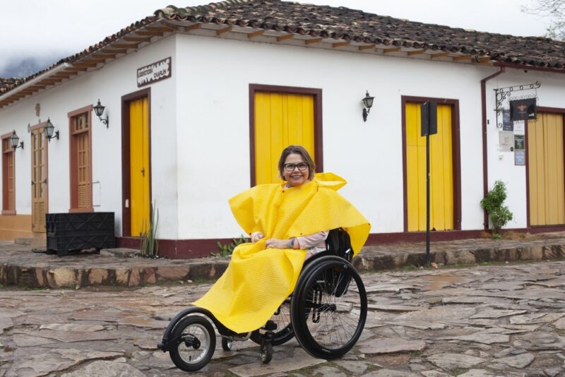 Laura usa sua cadeira de rodas, mas, na frente, acoplou um roda extra, que se chama Freewheel. Ela eleva as rodas dianteiras da cadeira, fazendo com que a circulação em pisos difíceis seja facilitada