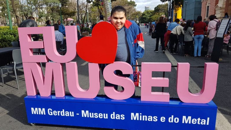 Criança com deficiência no museu: na foto, Mariana atrás de um monumento com a frase "Eu amo museu"