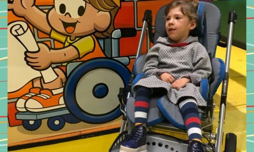 Lazer para crianças com deficiência: Alice está em um carrinho de bebê ao lado de um painel com personagem da Turma da Mônica
