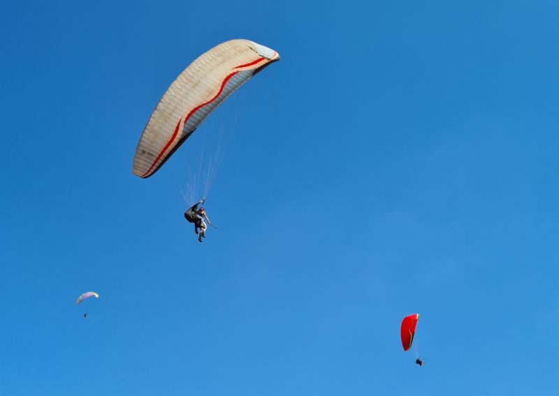 A foto mostra dois parapentes contra o céu azul brilhante no Topo do Mundo