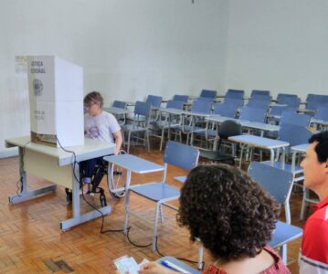 Laura está de cadeira de rodas, em uma seção de votação, numa escola. A foto da assessoria de imprensa do tre-mg registra uma simulação de voto.