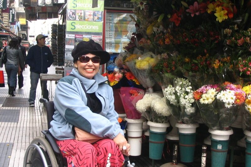 Laura está em sua cadeira de rodas, ao lado de uma banca de flores, na Calle Florida