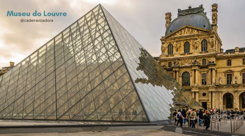 A pirâmide de vidro é vista em primeira plano, com o edifício do museu ao fundo.